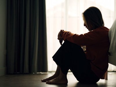 Silhouette of a woman sitting on the floor with her arms around her knees
